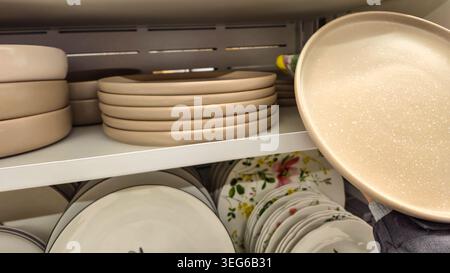 A collection of kitchenware, including plain beige plates and bowls, and decorative floral patterned plates, neatly arranged on store shelves Stock Photo