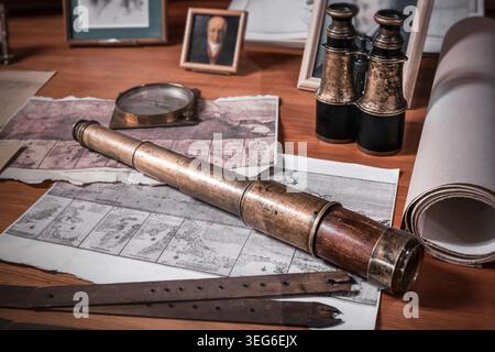 Antique spyglass, vintage nautical maps, compass and navigation instruments arranged on wooden explorer desk in historic interior. Atmospheric concept Stock Photo