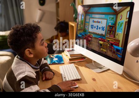 Black boy studying math lesson on desktop computer at home, engaging in online learning and digital education. Useful for homeschooling, edtech, remote school concepts Stock Photo
