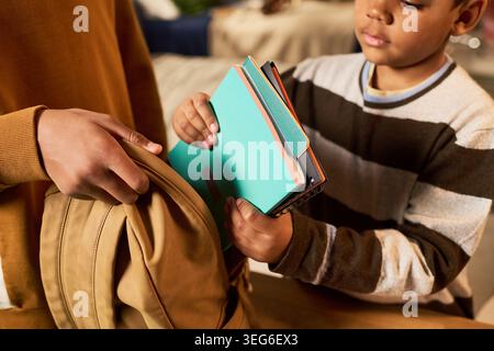 Black child packing notebooks into backpack with parent helping, preparing for school routine and learning. Education concept for back to school, parenting, childhood development Stock Photo