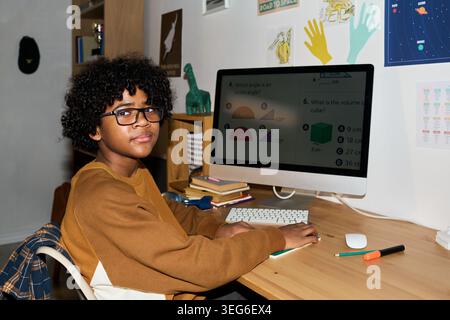 Portrait of Black teenager studying math on desktop computer at home, following online lesson and doing homework. Useful for remote learning, homeschooling, education technology Stock Photo