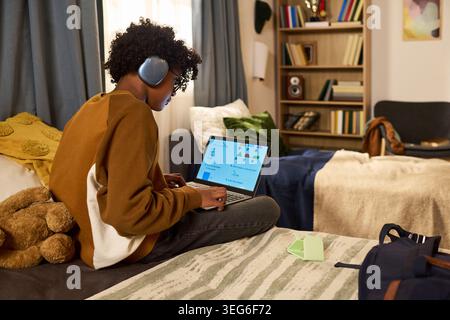 Teenager boy wearing headphones and using laptop for online learning in bedroom, studying geometry lesson and remote education concept. Side view for edtech, homeschooling marketing Stock Photo
