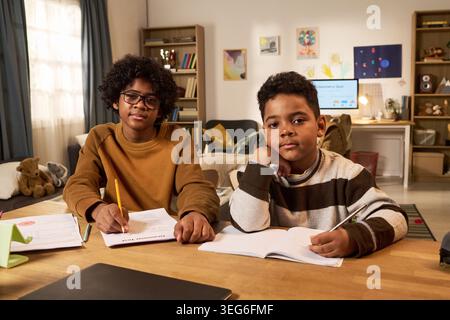 Portrait of two boys studying at home, writing in notebooks at shared desk during remote learning. Education support concept for homeschooling, tutoring, child development Stock Photo