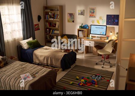 Wide angle shot of kids bedroom featuring computer displaying geometry quiz, study desk, books, toys, supporting homeschooling, online learning, child education marketing Stock Photo