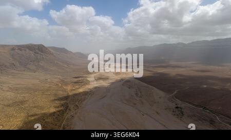 Aerial view of an arid desert valley with winding dry riverbed, rugged mountains on both sides, and dramatic clouds casting shadows across the landsca Stock Photo