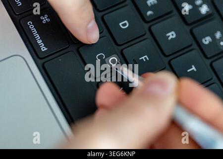 Hands applying letter stickers with tweezers on an English keyboard, adding Cyrillic alphabet characters for multilingual typing Stock Photo