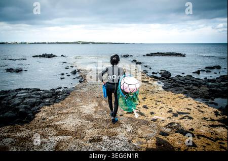 Haenyeo diver walking down a rocky pier to the sea Stock Photo