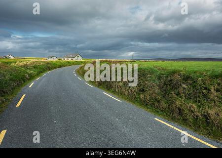 Narrow winding country road through green fields in the Dingle Peninsula Kerry Ireland under a stormy sky. Stock Photo