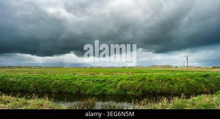 Dramatic dark clouds and rain shafts over green fields and a small river in the Dingle Peninsula Kerry Ireland. Stock Photo