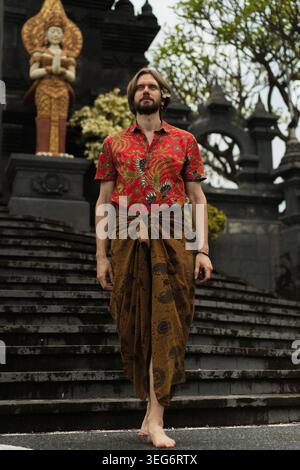Confident man in batik shirt and sarong at Balinese temple steps, Bali Stock Photo