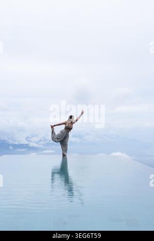 Woman practicing yoga balance pose at infinity pool, Munduk, Bali Stock Photo