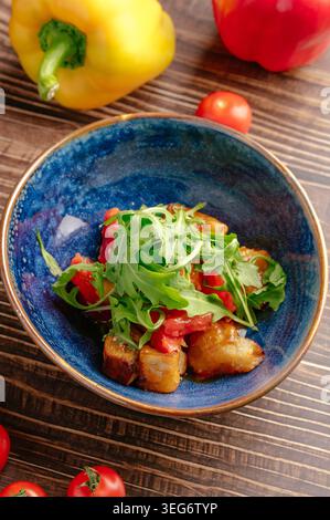 Warm eggplant salad with arugula and tomatoes in a blue bowl Stock Photo