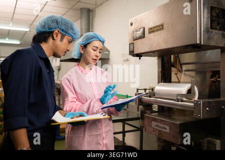 Two workers inspecting packaging machine and recording data in beverage production process Stock Photo