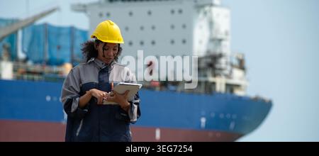 Female maritime engineer using digital tablet for logistics management and industrial port operations near cargo vessel Stock Photo