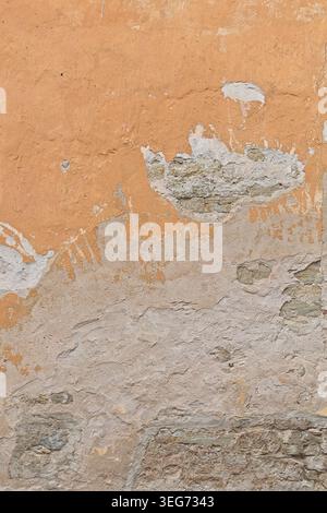 Deteriorating exterior wall with several visible layers of building materials with cracked and peeling plaster, exposing the rough stone underneath. Stock Photo