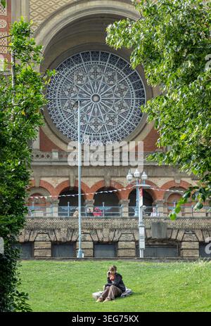 London, UK - Jun 09, 2025 - Engrossed in a mobile phone conversation, a young woman rests peacefully on the sweeping green lawn of Alexandra Palace, w Stock Photo