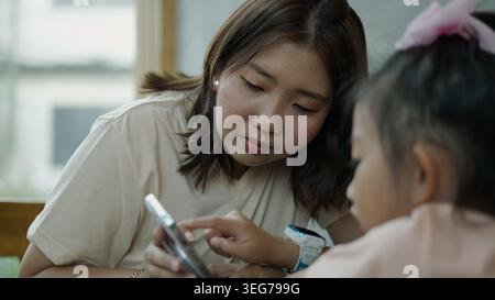 Mother teaching daughter using smartphone, digital education at home Stock Photo