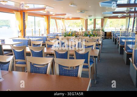 Modern restaurant area inside passenger sightseeing ship with rows of tables and chairs illuminated by natural daylight. Stock Photo