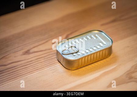 Small rectangular sardine tin with pull-tab resting on a warm wooden table, evoking Portuguese seafood tradition and simple packaging. A minimalist st Stock Photo