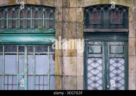 Weathered green doors and decorative ironwork on a historic stone façade, featuring peeling paint, cracked panes and textured masonry that evoke vinta Stock Photo