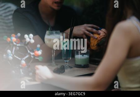 School friends discussing science over drinks with a brain model and molecular kit at a cafe table Stock Photo