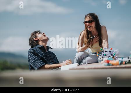 Two friends laughing outdoors while studying with a molecular model on a sunny day Stock Photo