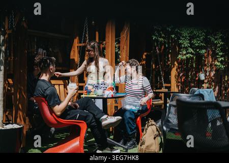 School friends hanging out at an outdoor cafe table sharing snacks and drinks on a sunny day Stock Photo