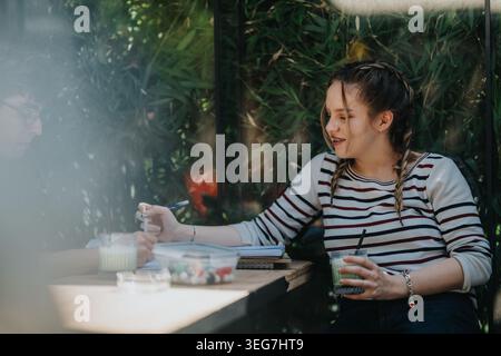 Two school friends studying and drinking smoothies at an outdoor cafe table during break Stock Photo