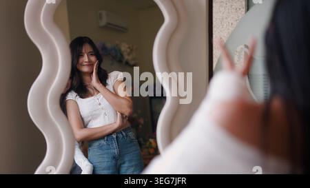 Young asian woman smiling, seeing reflection while posing in decorative mirror Stock Photo