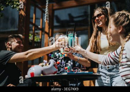 School friends clinking colorful drinks and laughing outdoors at a sunny gathering Stock Photo