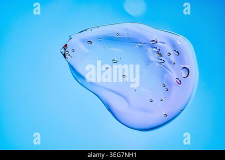 Pink-blue gel droplet with scattered bubbles, soft smooth texture and glossy translucent surface. Clean abstract close-up with bright blue background. Stock Photo