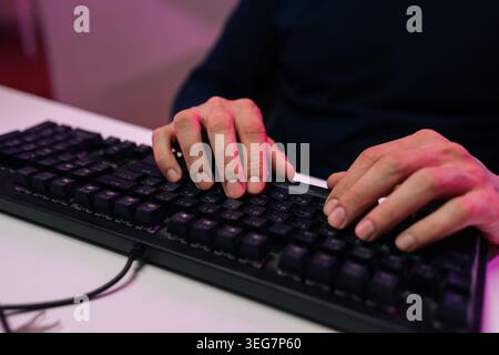 Close-up of male hands typing on black computer keyboard. Moody scene with pink neon lighting. Concept of programming, coding, hacking, cybersecurity Stock Photo