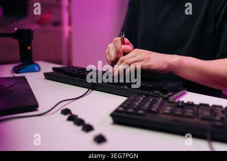 Technician hands changing mechanical switches on black computer keyboard, performing maintenance and repair work on electronic gadget placed on desk Stock Photo