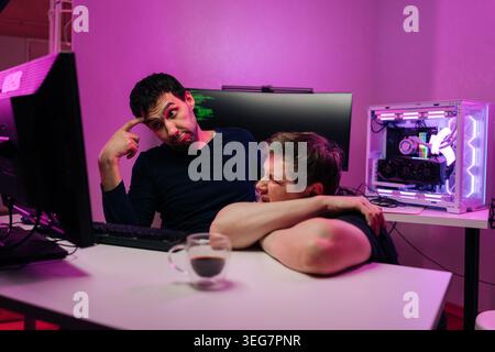 Two male developers experiencing stress and frustration from coding issues and tech burnout working in modern office with vibrant neon lighting Stock Photo