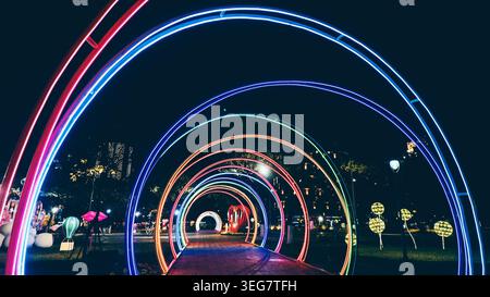 colorful neon light tunnel with glowing rainbow arches and futuristic night perspective, illuminated LED walkway with vibrant festive decoration and Stock Photo