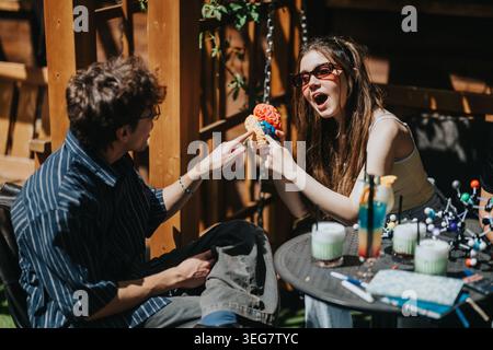 Two school friends examining a colorful brain model while chatting at an outdoor study table Stock Photo