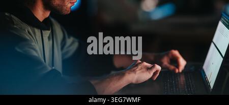 Business teammate working late on laptop analyzing data and typing on keyboard in low light Stock Photo