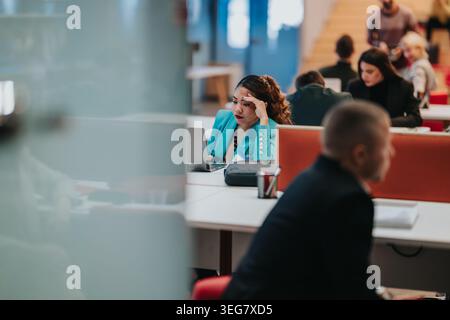 Businesswoman working on laptop in open office surrounded by coworkers in a collaborative workspace Stock Photo