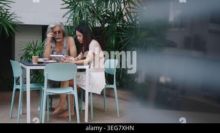 Intergenerational duo discussing on tablet, older man learning from young woman Stock Photo