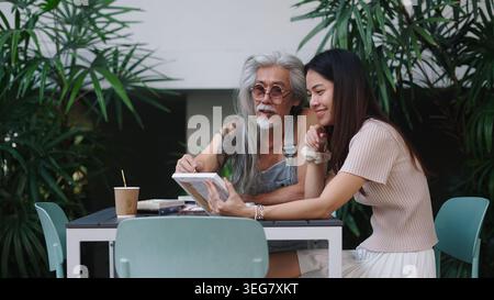 Senior man and young woman discussing art, sharing creative ideas at outdoor cafe Stock Photo