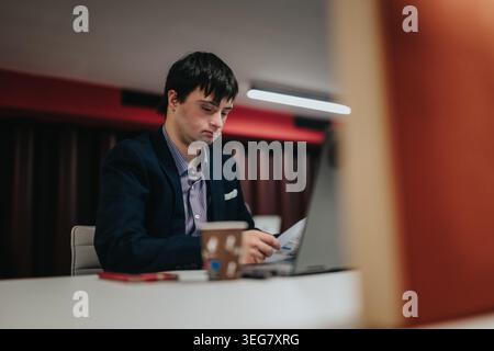 Businessman with Down syndrome working on laptop in modern office while reviewing documents Stock Photo
