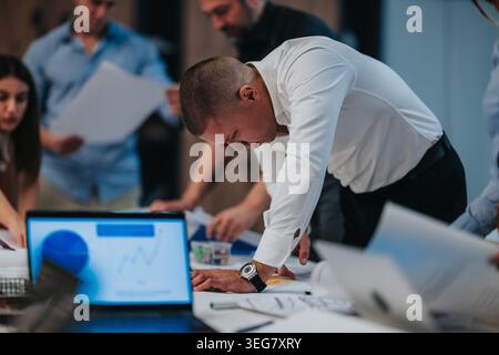 Business team collaborating around a table reviewing charts, documents and laptop during a planning session Stock Photo