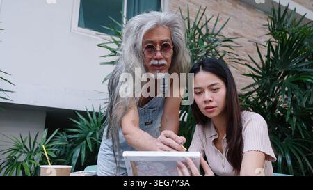 Senior man teaching young woman painting, sharing creative knowledge and skill Stock Photo