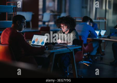 Young business teammates working late on laptops in a modern coworking space Stock Photo