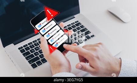 Person receives scam messages on their phone while using a laptop at home Stock Photo