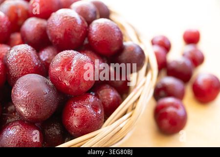Fresh Governor's Plum Flacourtia Indica Red Exotic Berries in Wicker Basket on Wooden Table Stock Photo