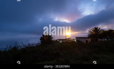 Lighthouse illuminating the sky with bright beam during an overcast dusk in Madeira island. Stock Photo