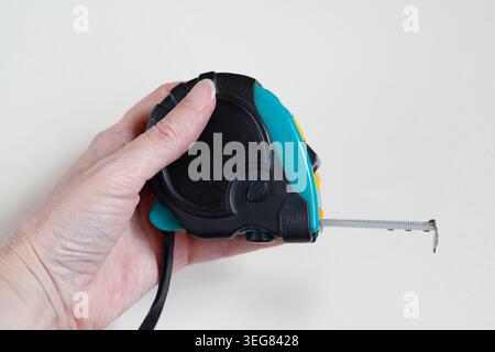 Tape measure. Metal industrial construction tape centimeter measure close up. Human hand holds a black and green a flexometer and measuring tape. Stock Photo