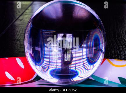 A solid glass ball on a dark surface captures reflected light. Stock Photo