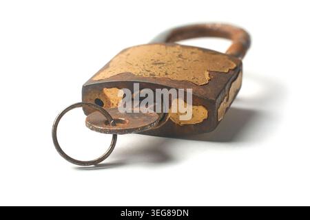 old weathered rusty iron padlock with peeling gold paint and metal key inserted into keyhole isolated white background, soft focus with shadow Stock Photo